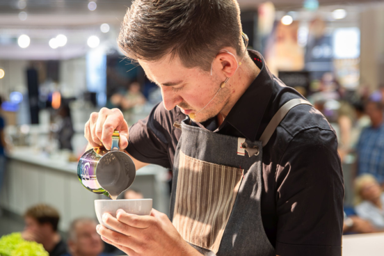 Junger Barista füllt kunstvoll Milchschaum in Cappuccinotasse | © Congress Messe Innsbruck Junger Barista füllt kunstvoll Milchschaum in Cappuccinotasse | © Congress Messe Innsbruck